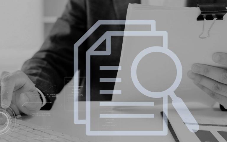 grayscale image of man's hand typing on computer while holding paper