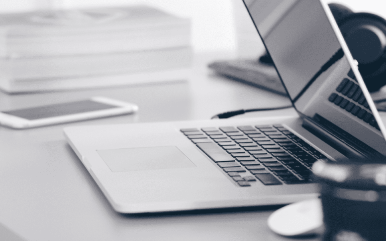 A picture of a desk with a laptop halfway open, a phone and books