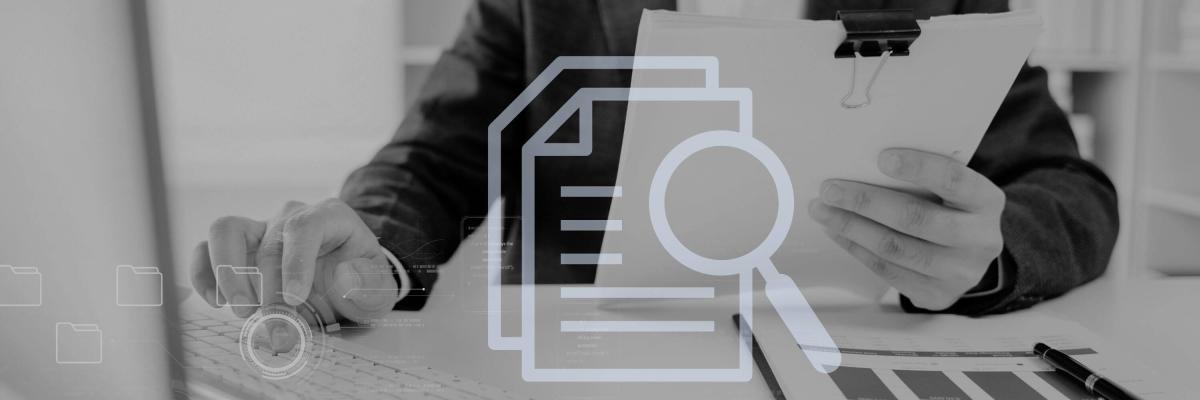 grayscale image of man's hand typing on computer while holding paper