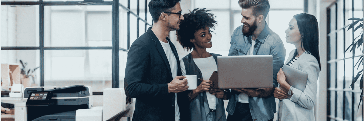 Four people gathering around a laptop with the Xerox VersaLink C7125 in the background